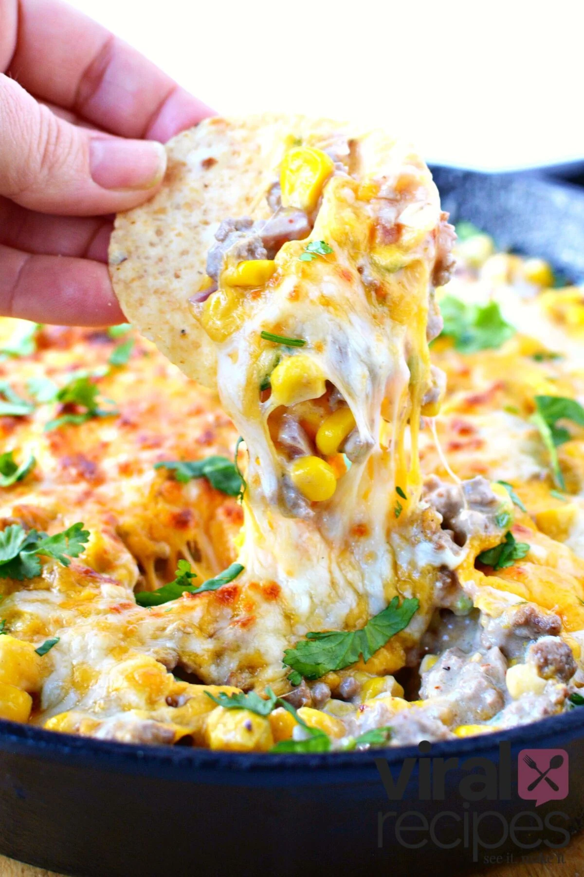 chunky warm elote dip with beef being dipped with tortilla chip.