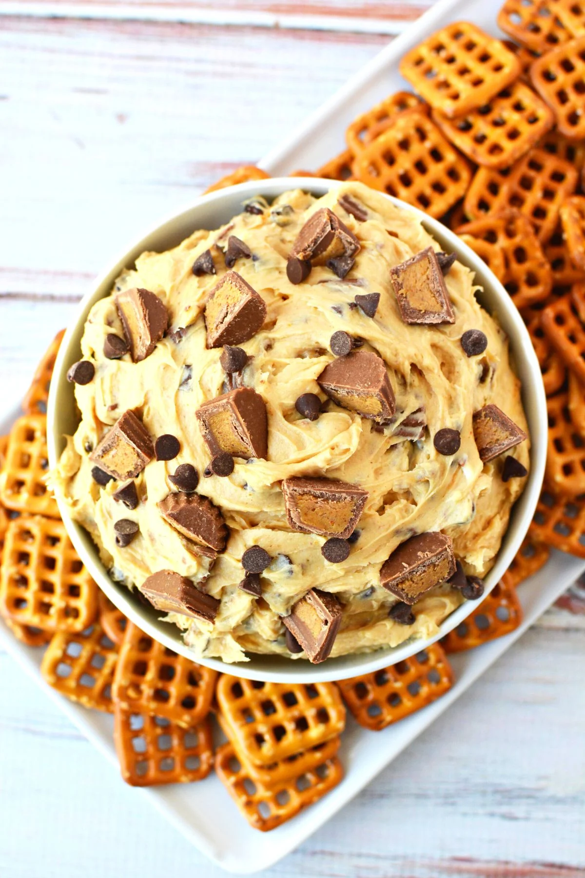 large bowl of dessert dip surrounded by pretzels.