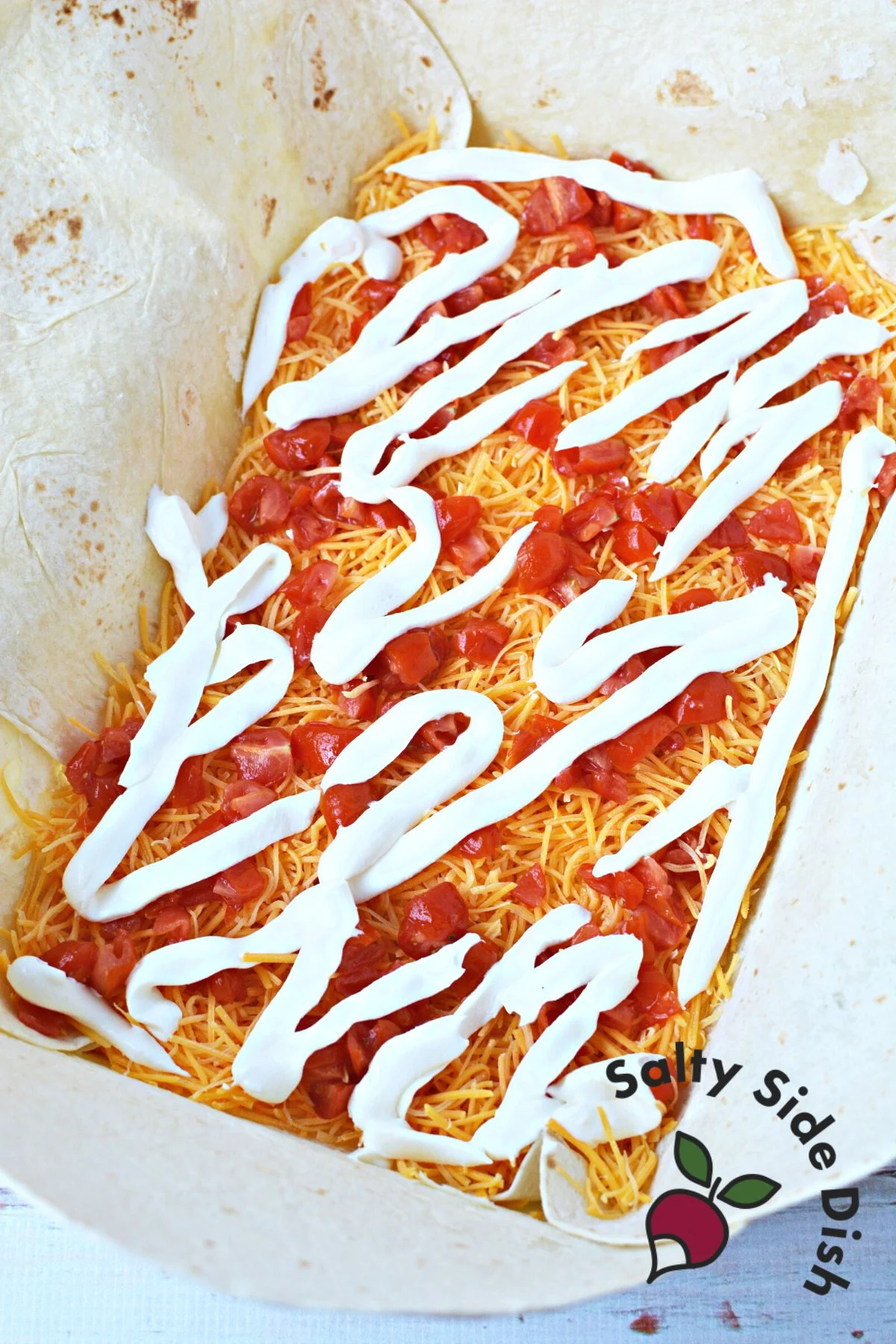 adding shredded cheese, diced tomatoes, and sour cream to bottom of flour tortillas.