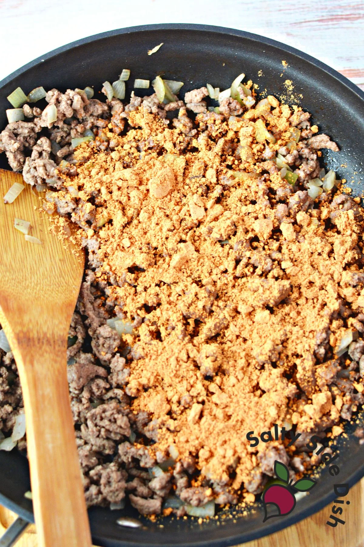 adding taco packet seasoning to ground beef in a nonstick skillet