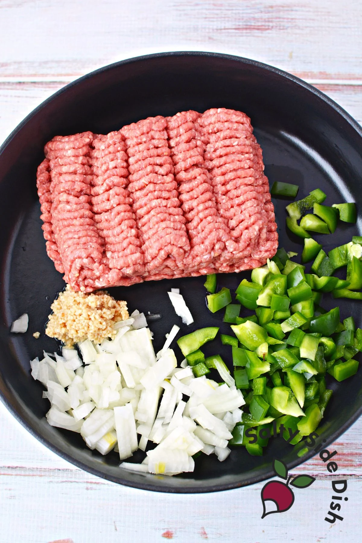 ground beef, onions, garlic, and green peppers in a cast iron pan.