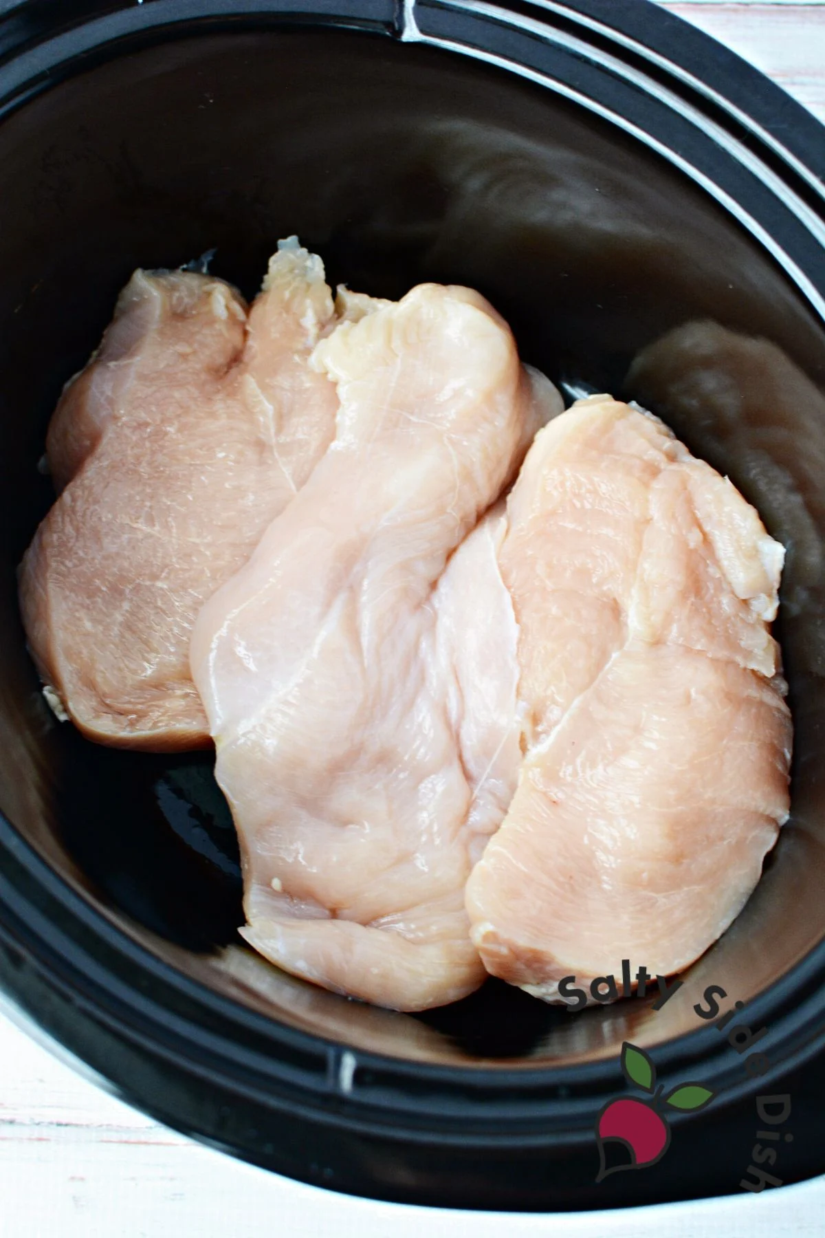 defrosted chicken breasts in the bottom of a black slow cooker.