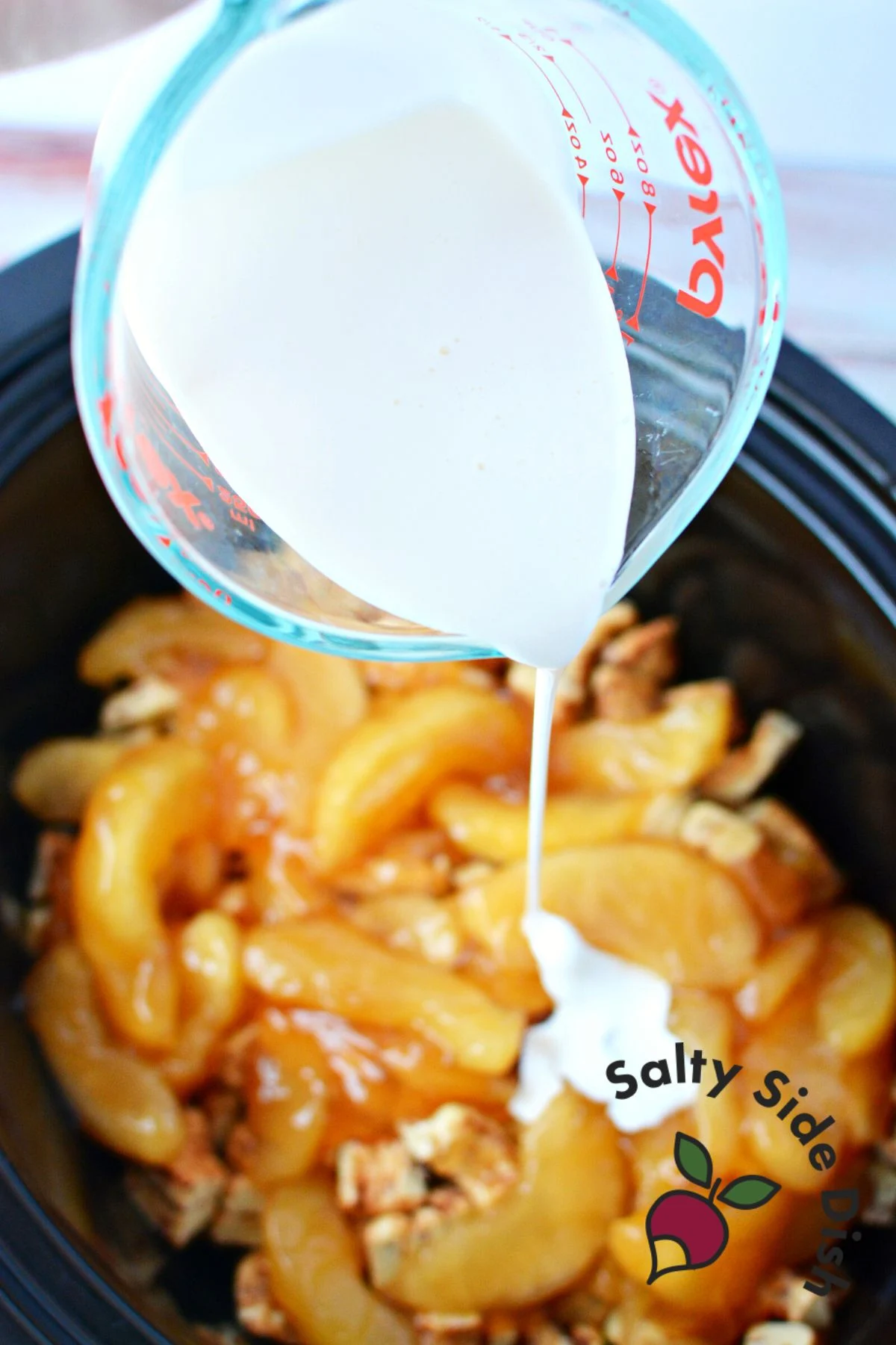 heavy whipping cream being poured over apple pie filling.