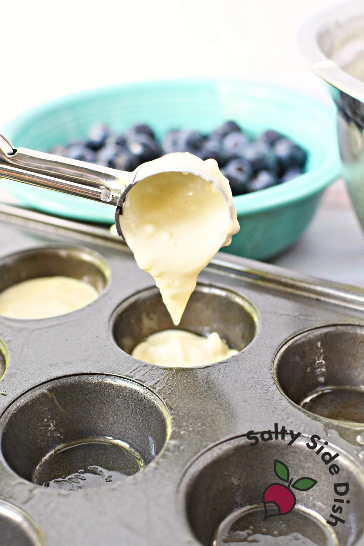 adding pancake batter to a mini muffin tin using a 1 tablespoon scoop.