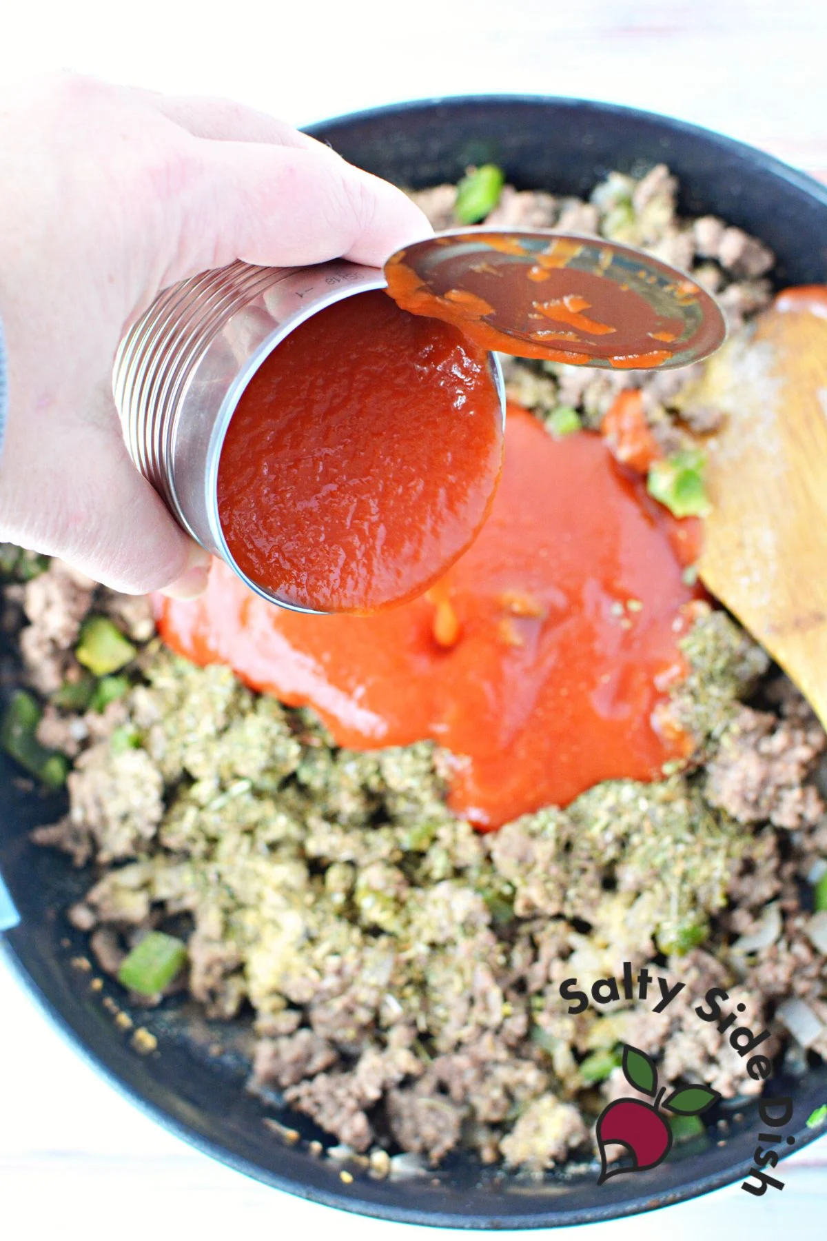 pouring canned tomatoes into beef in cast iron pan.