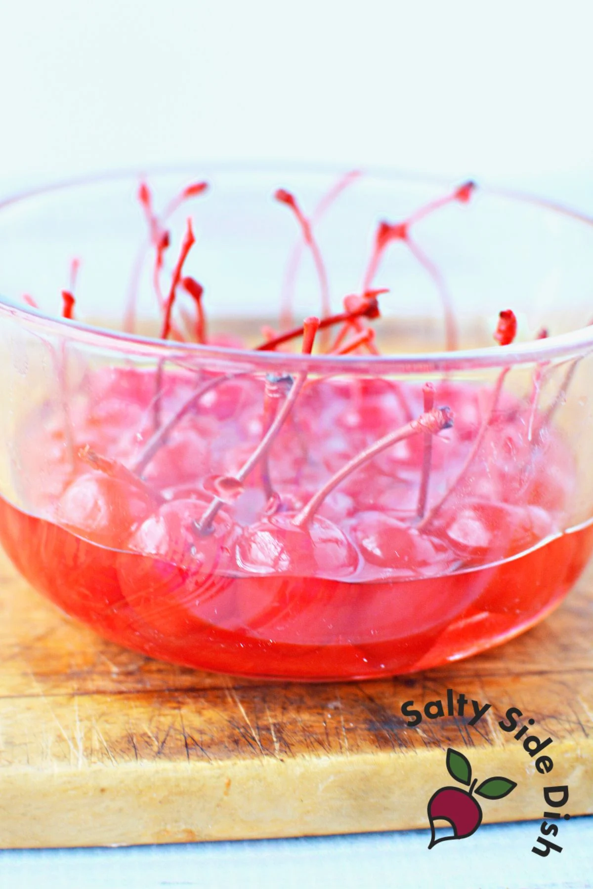 cherries with stems sitting in a bowl of vodka.