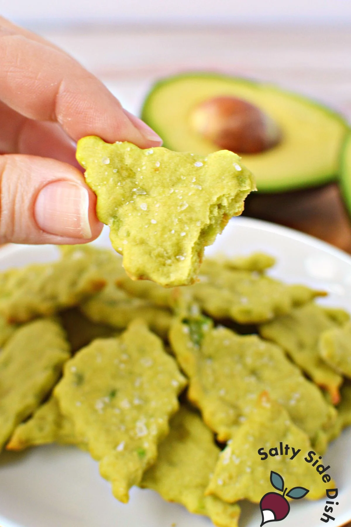 baked avocado cracker being held with a bite out of it.