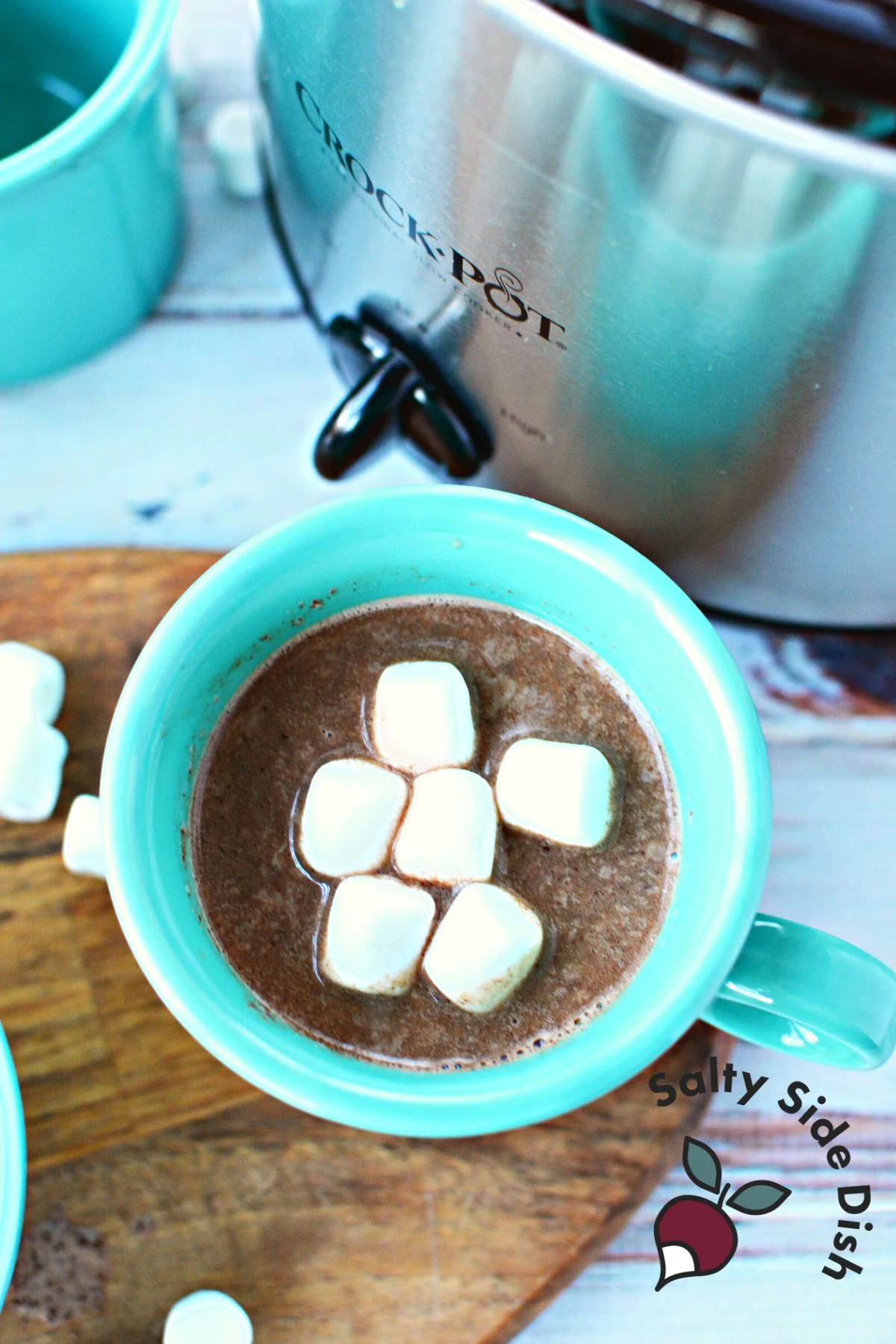 hot chocolate with marshmallows in a blue mug sitting by a crock pot.