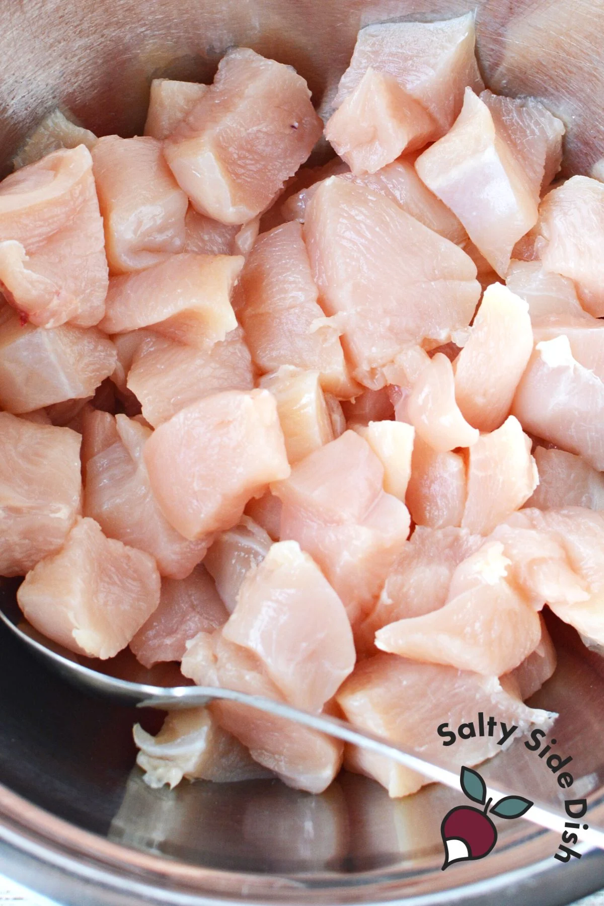 raw cut up chicken breasts in a mixing bowl uncooked.