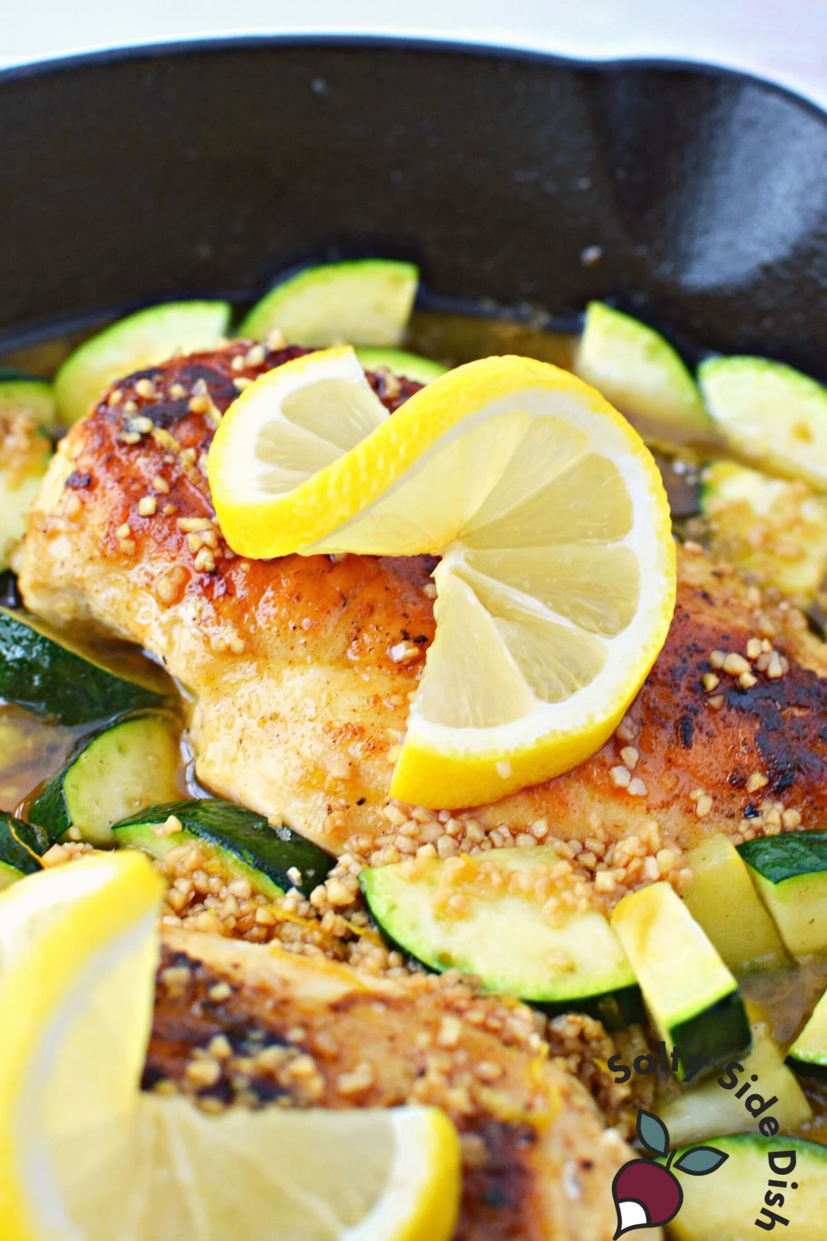 chicken breast with twisted lemon on top sitting in cast iron pan.