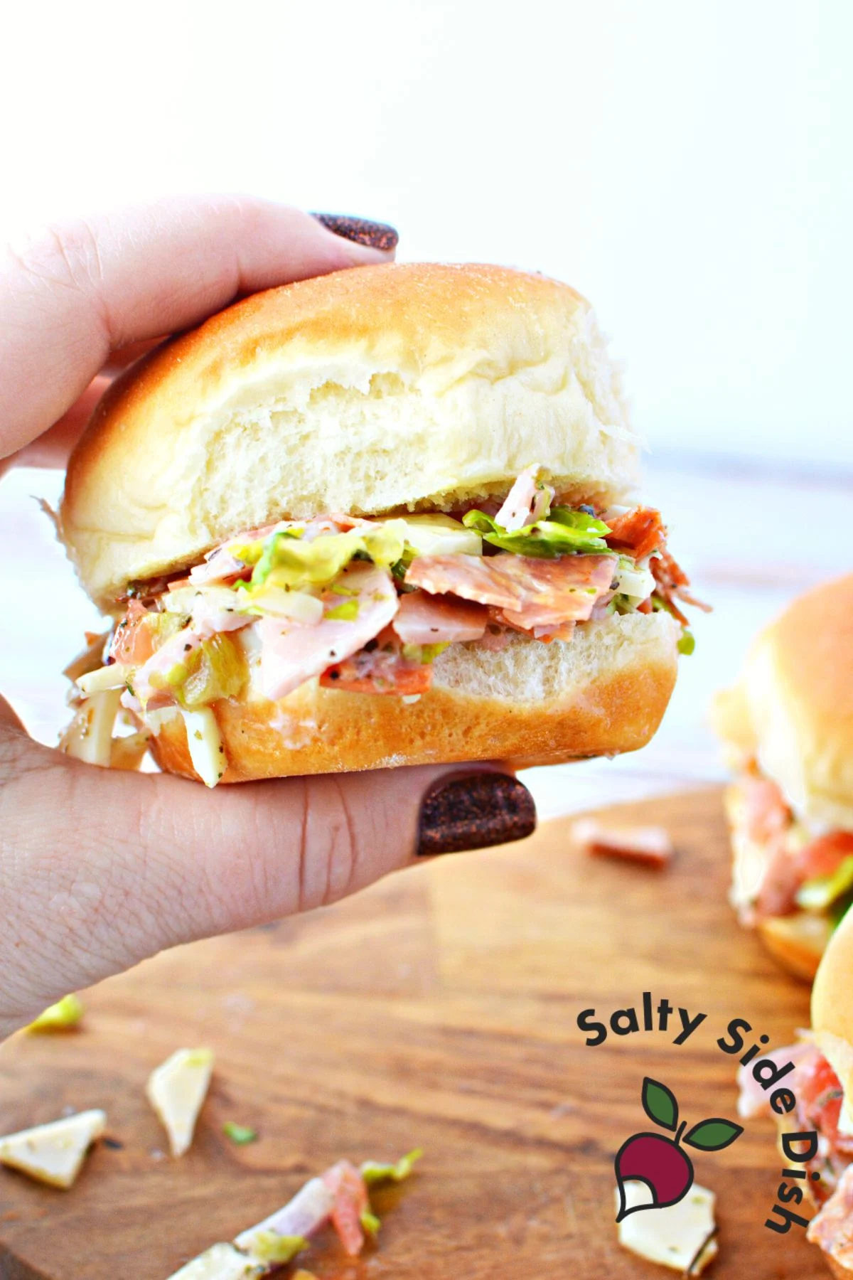 grinder ingredients chopped and served on a kings hawaiian roll being held in a hand.