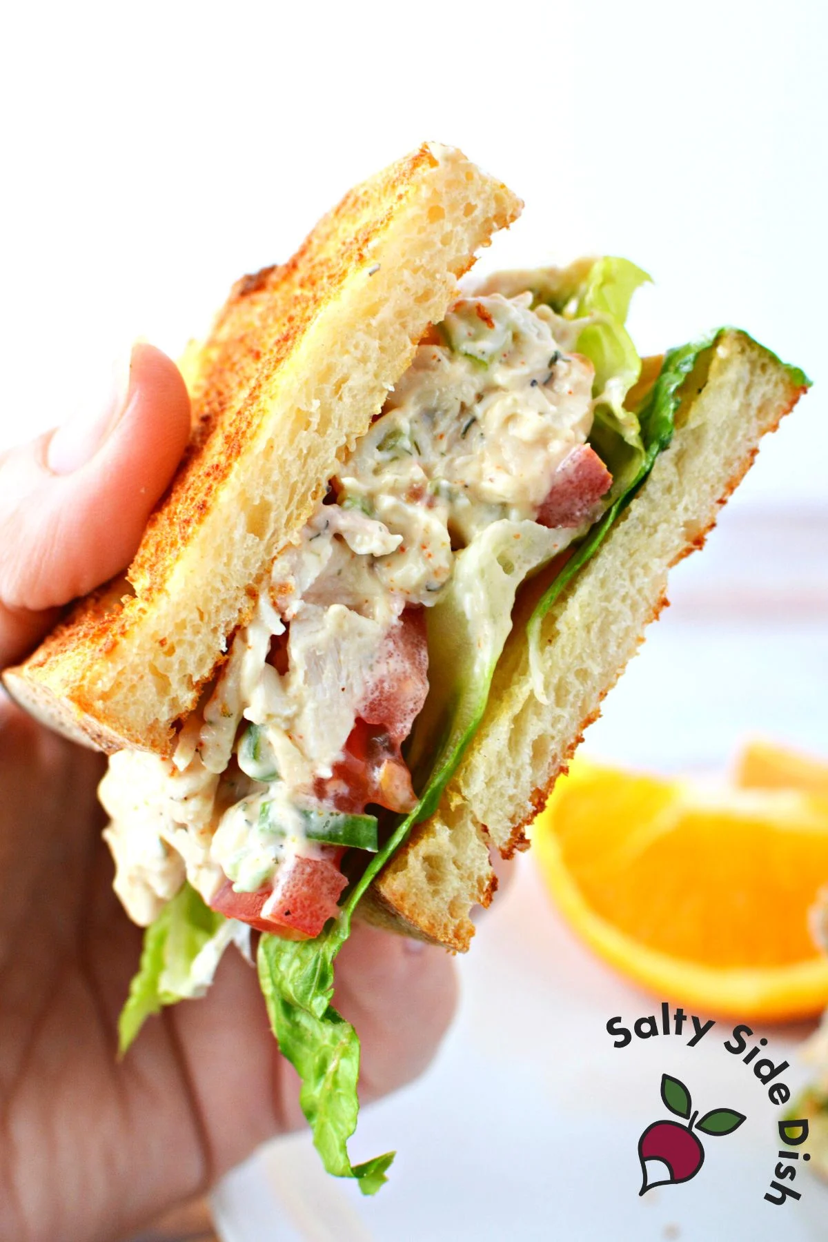 chicken salad sandwich being held in the air and all layers visible.