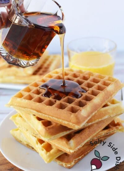 pouring syrup over stack of homemade waffles.