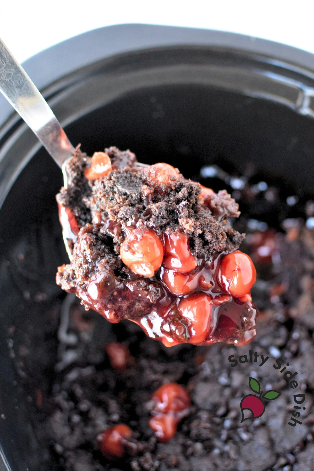 a spoon with a scoop of chocolate cherry dump cake coming out of a slow cooker.