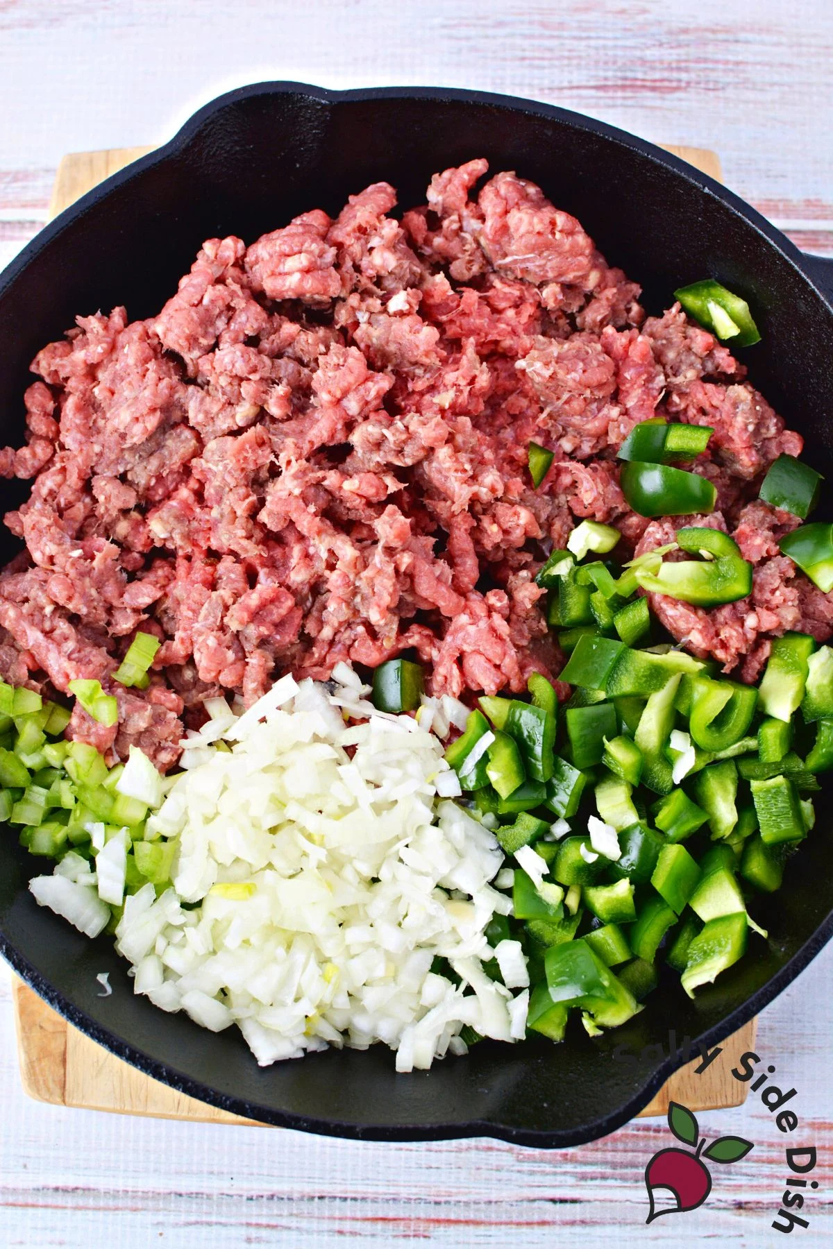 raw ground beef, diced onions, and diced green peppers in a cast iron pan.