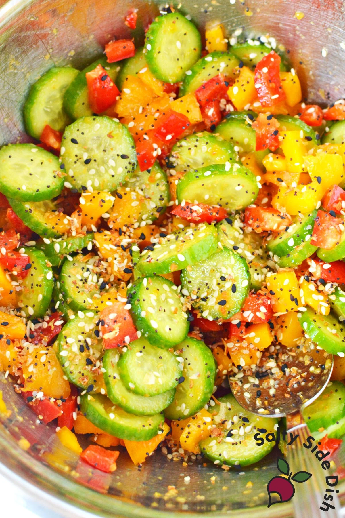 pouring everything bagel on a salad in a mixing bowl.