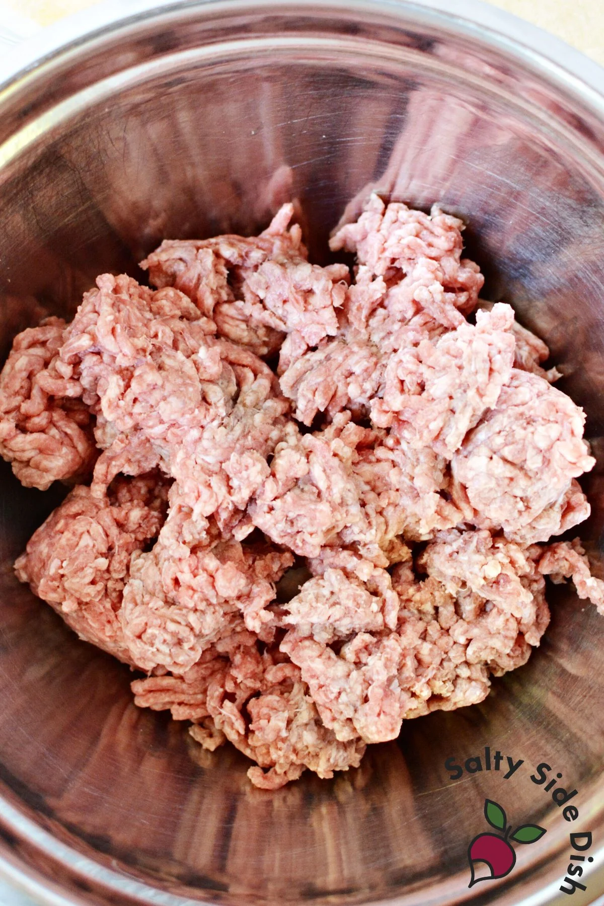 Raw ground beef mixed with garlic powder onion powder salt and pepper in metal bowl