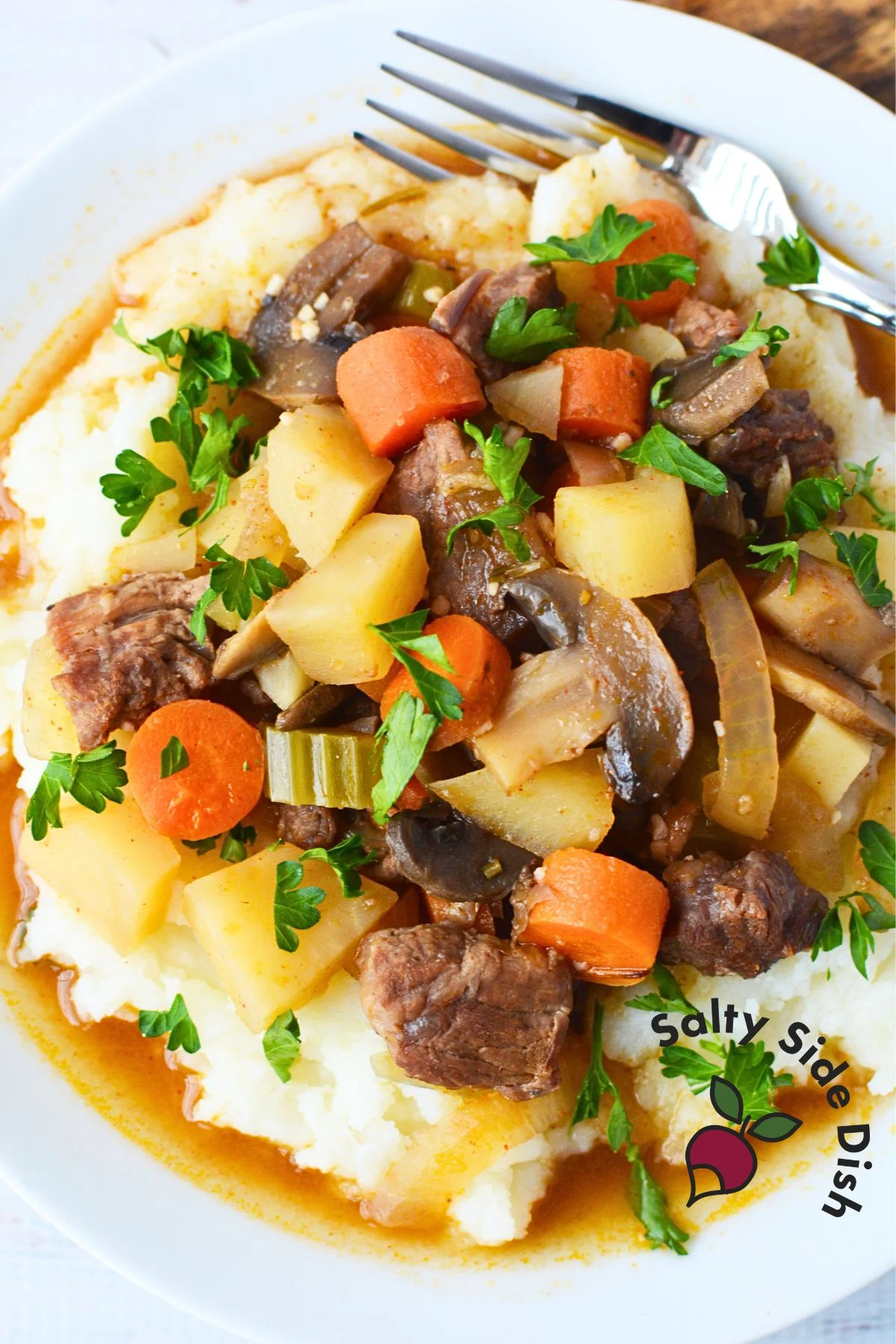 large plate of mashed potatoes, stew, and a fork on the side.