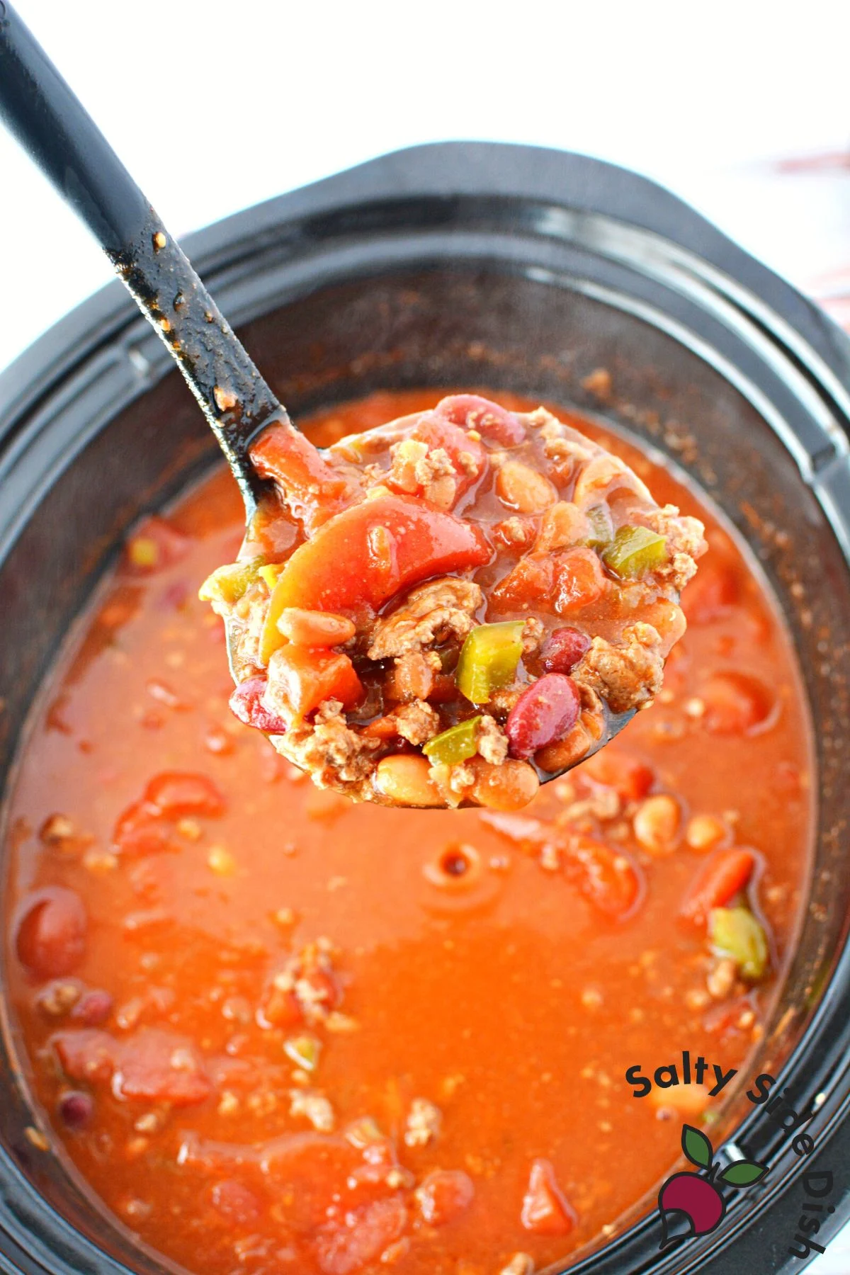 chili in a slow cooker with a close up of chili in a ladle.