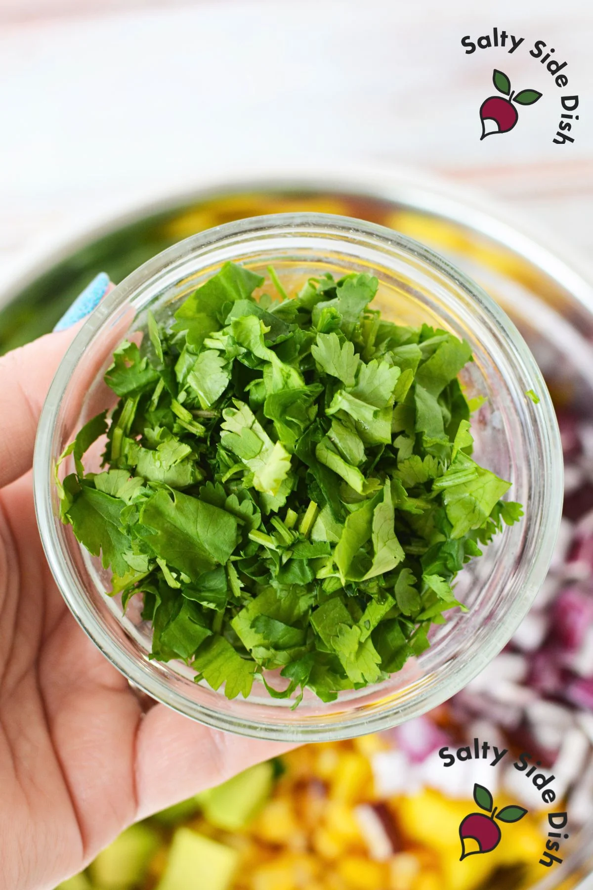 A bowl filled with fresh, green cilantro leaves, ready to be used as an ingredient or garnish in various dishes, including Pineapple Mango Fruit Salad.