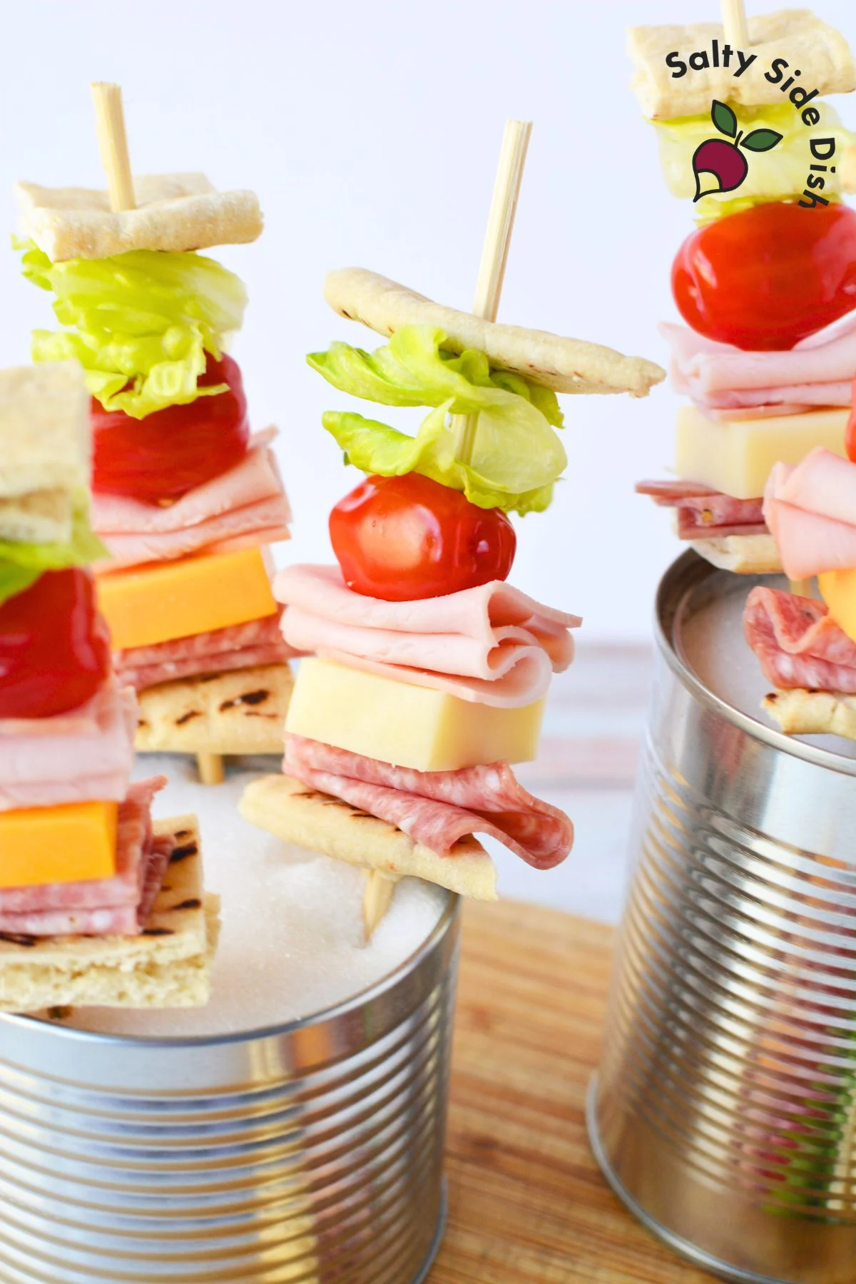 Sandwich skewers displayed upright in two cans filled with granulated sugar, one a recycled soup can and the other a decorative metal can.
