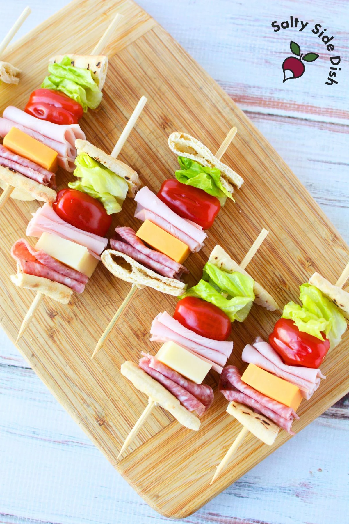 Close-up view of a sandwich skewer, showing the details of the layered ingredients including pita bread, lettuce, tomato, ham, cheese, and salami.