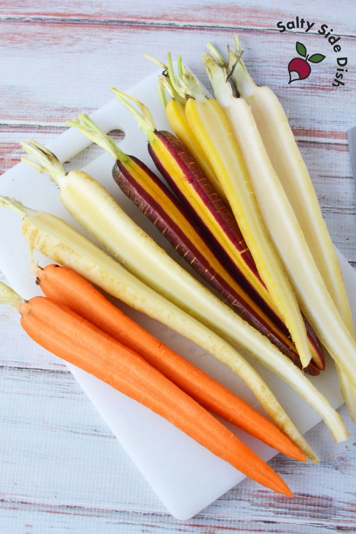 pile of rainbow carrots on a cutting board cut in half lengthwise.