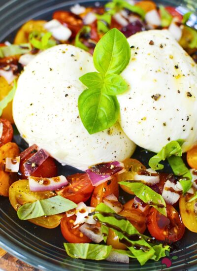 fresh burrata salad recipe on a plate with cheese, tomatoes, basil, and red onions.