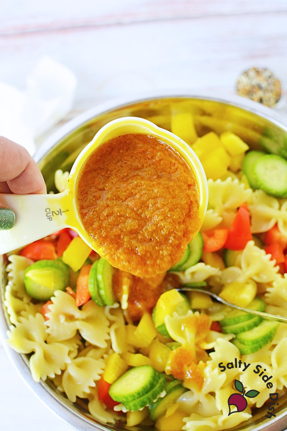 Mixing pasta with cucumbers and bell peppers and ginger dressing.