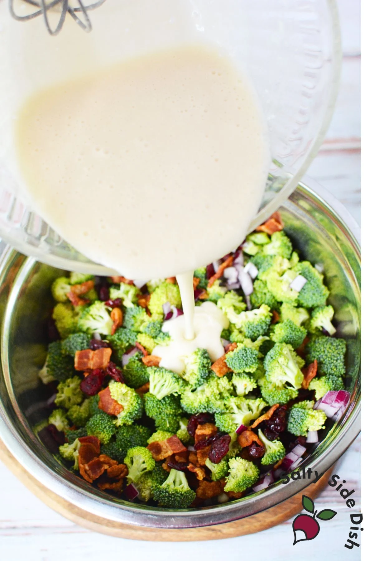 pouring broccoli salad dressing over ingredients in a bowl.