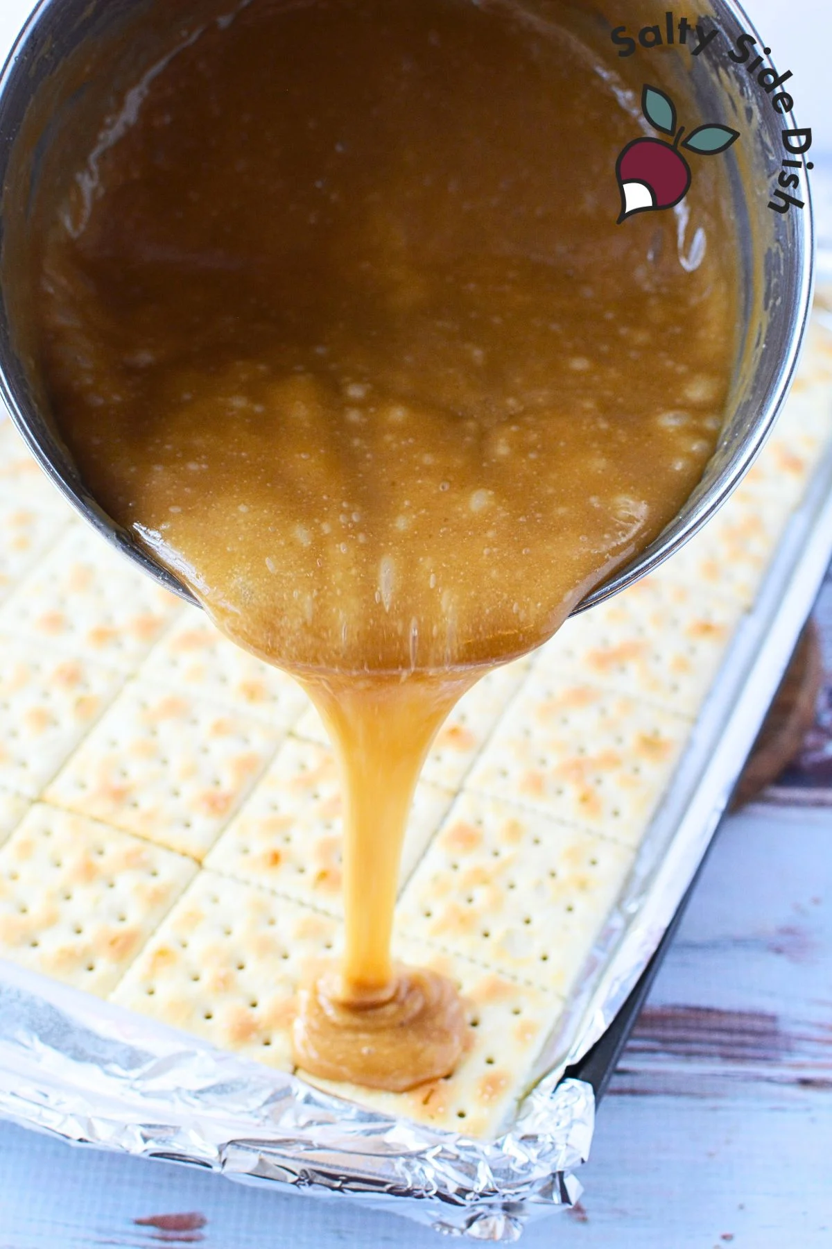 Pouring golden caramel toffee over a layer of saltine crackers, creating the base for Christmas Crack.