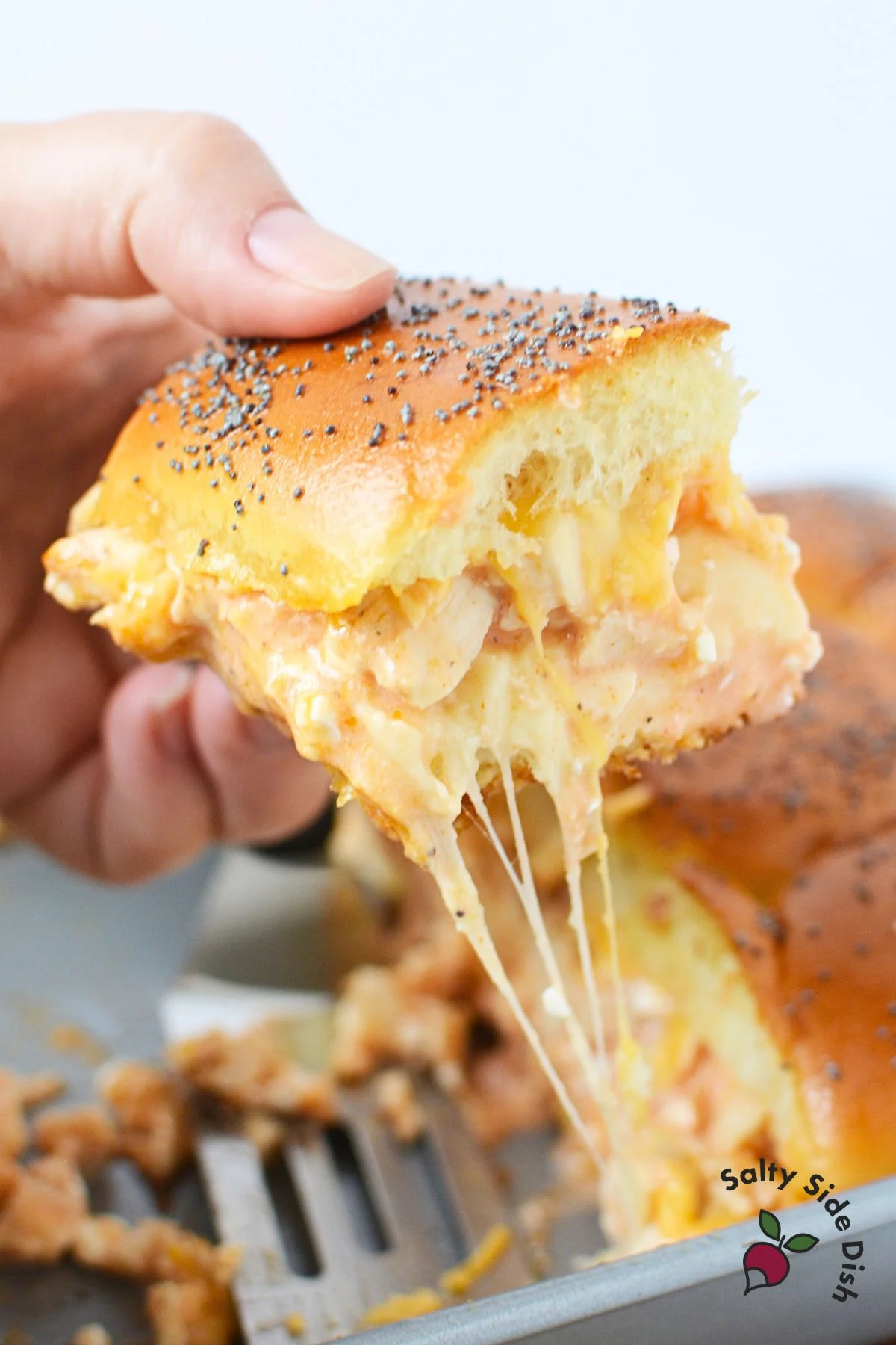cheesy buffalo chicken sliders being pulled out of a baking pan.