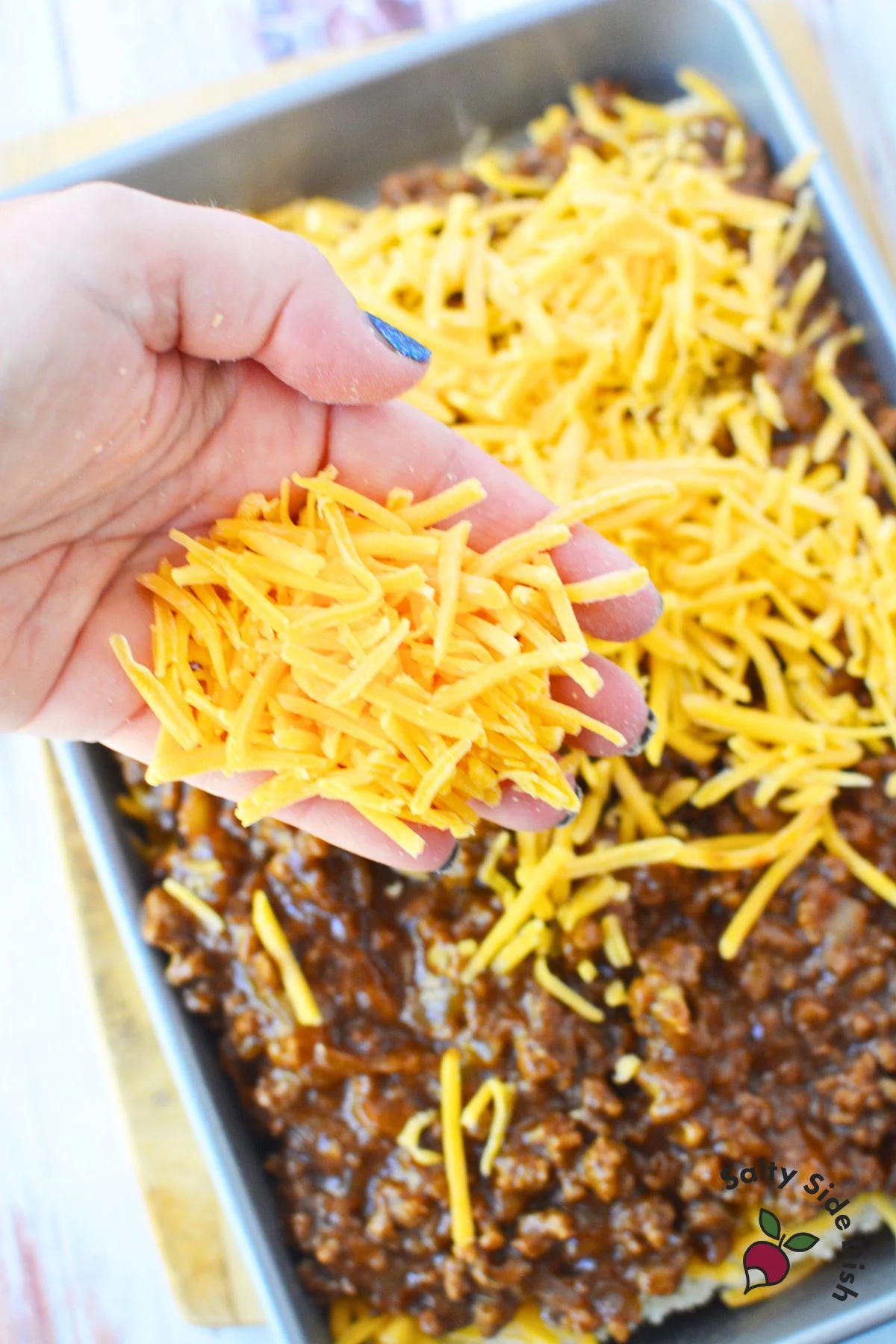 adding shredded cheddar cheese to sloppy joe meat mixture.
