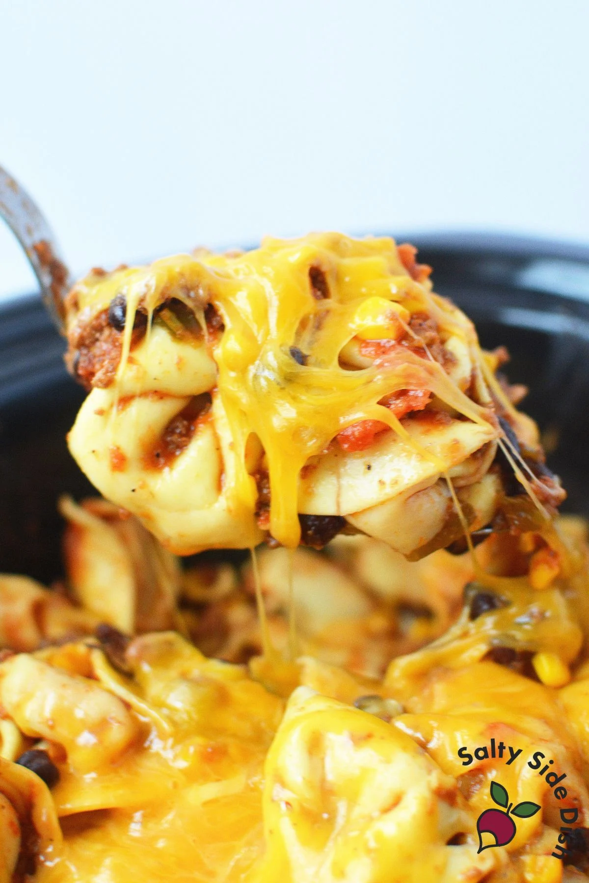 Easy one-pot taco tortellini being scooped from a slow cooker.