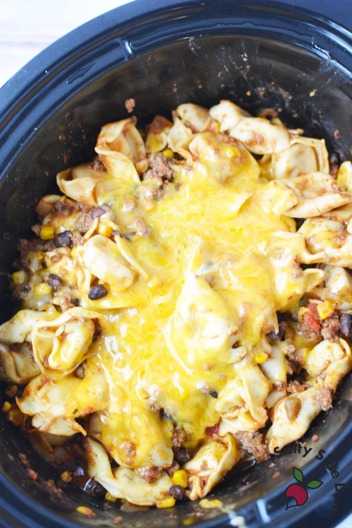 Cheesy taco tortellini in a slow cooker with melted cheese on top.