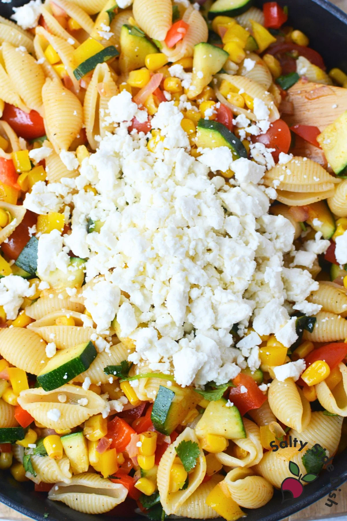 adding feta cheese to the pasta salad recipe.