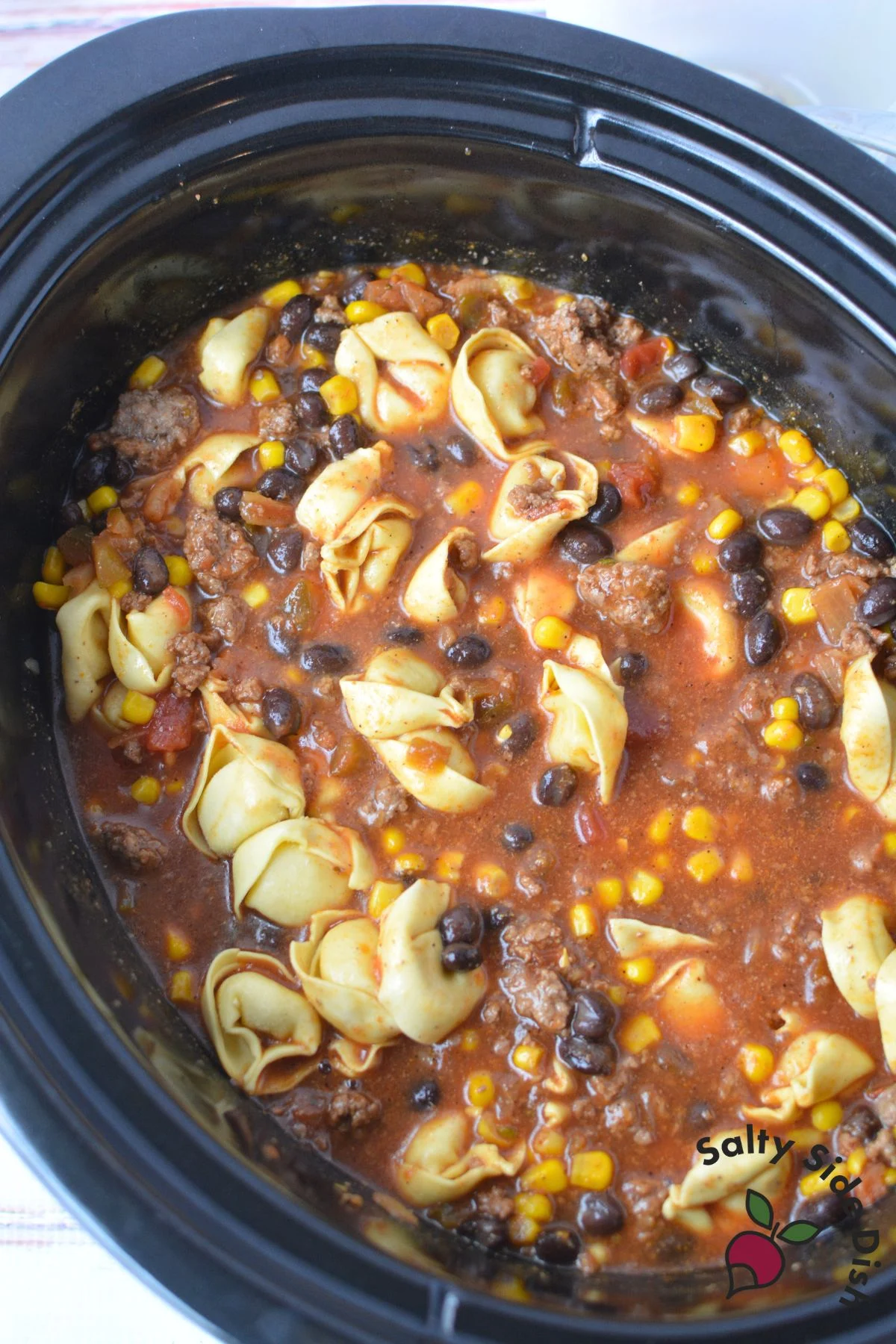 Cheese tortellini with taco-seasoned beef and salsa in a slow cooker.