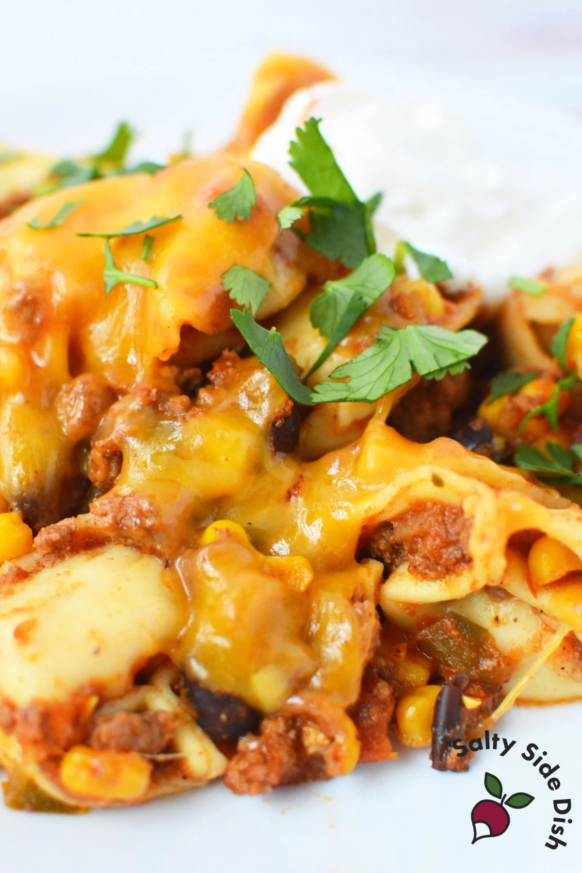 Slow Cooker Taco Tortellini on a plate topped with cheese, sour cream, and cilantro