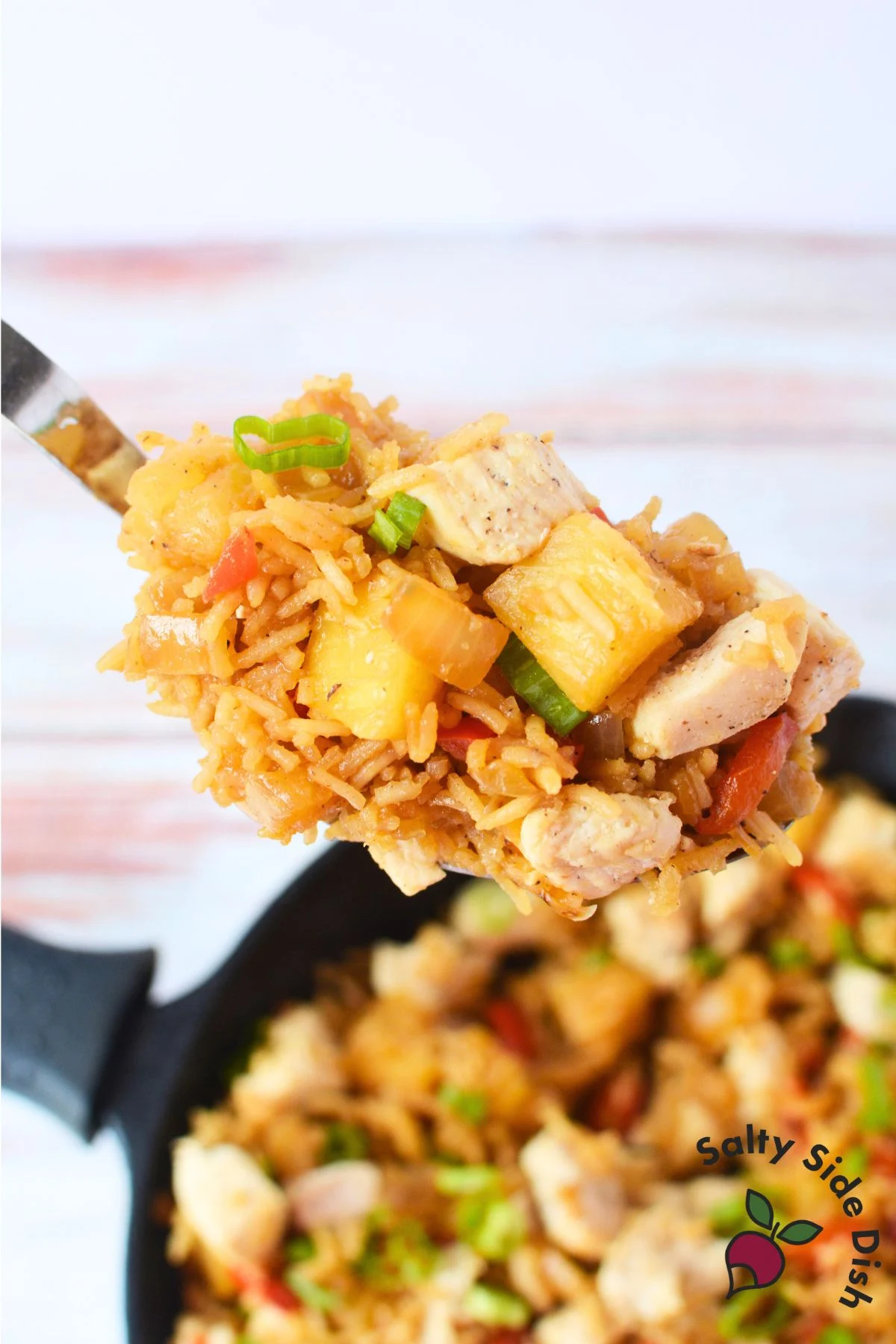 view of chicken and pineapple fried rice in a spoon, garnished with sliced green onions and pineapple chunks.