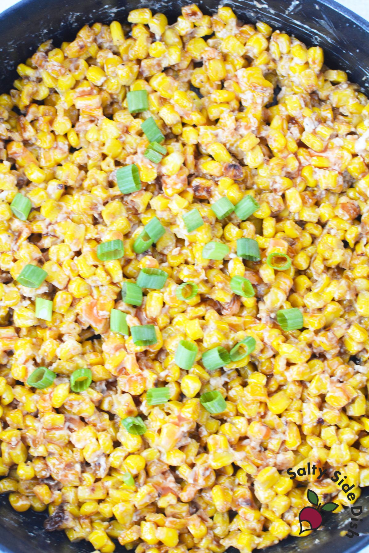 skillet corn ready to serve with sliced green onions on the top.