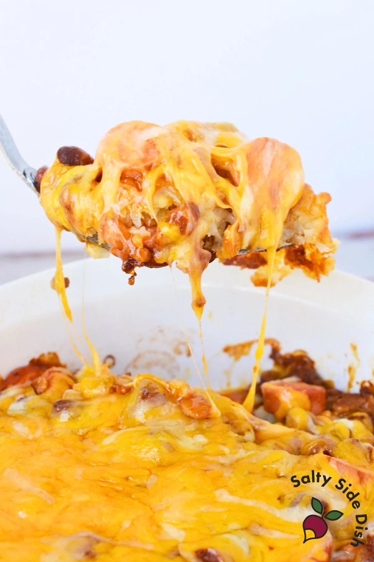 scoop of tater tot casserole with hot dogs in a serving spoon.