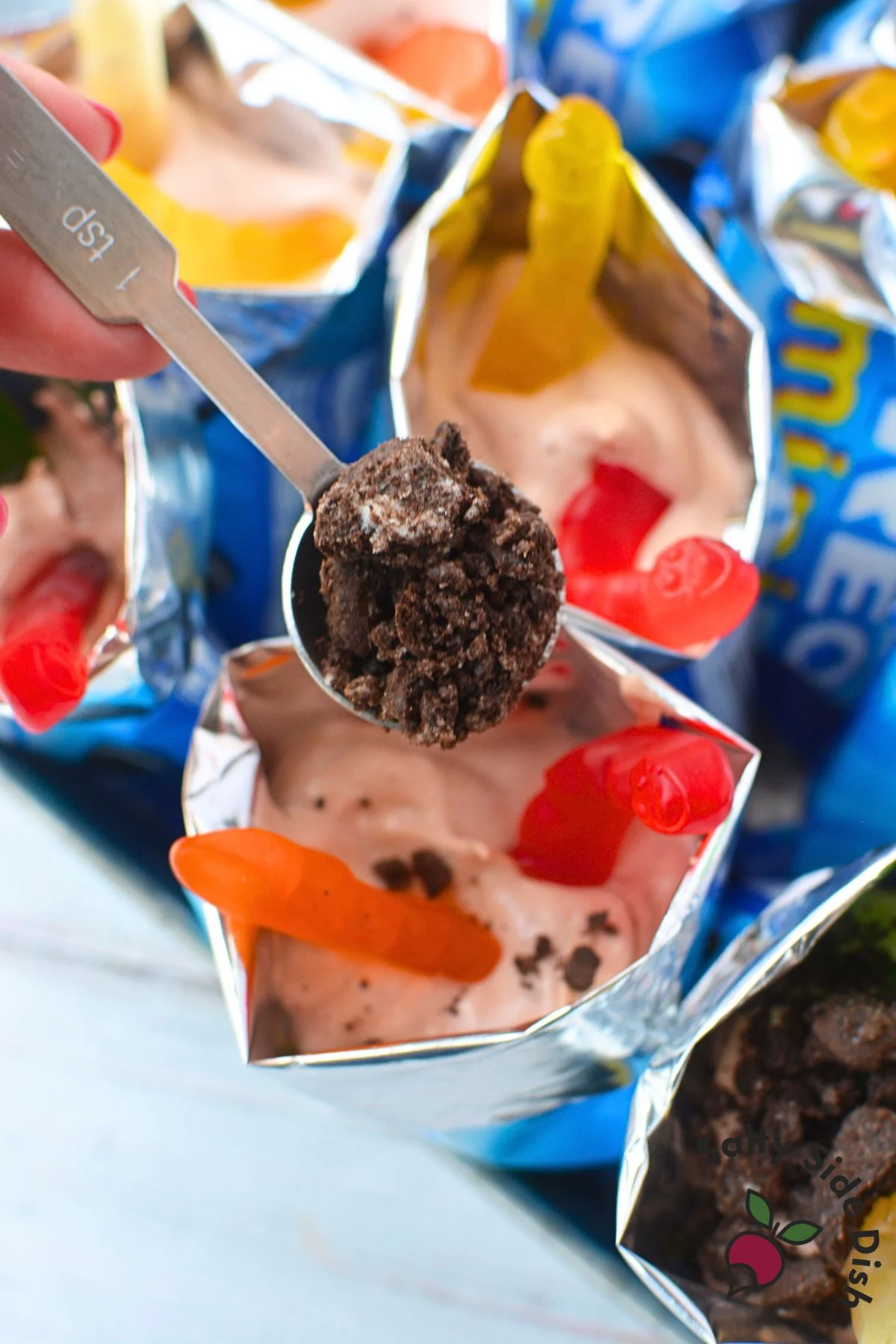 Sprinkling crushed Oreo cookies on top of dirt pudding cups with gummy worm decorations.