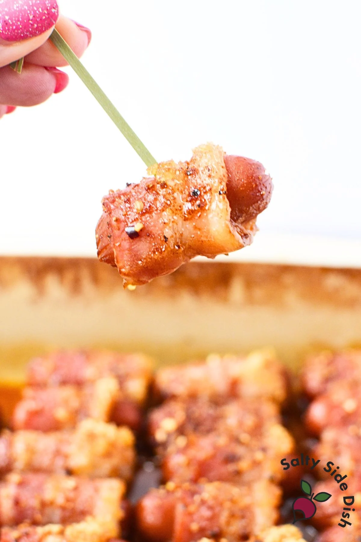 Single bacon-wrapped Li’l Smokie on a party skewer, held above pan.