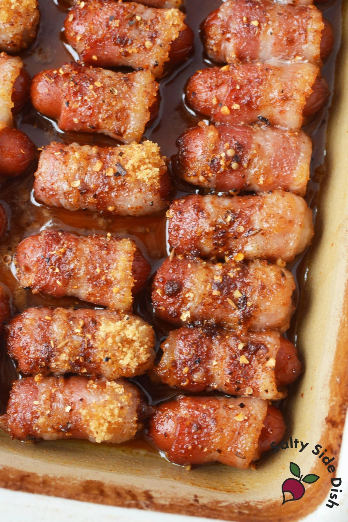Close-up of sticky, baked Li’l Smokies with crisped bacon in a baking dish.