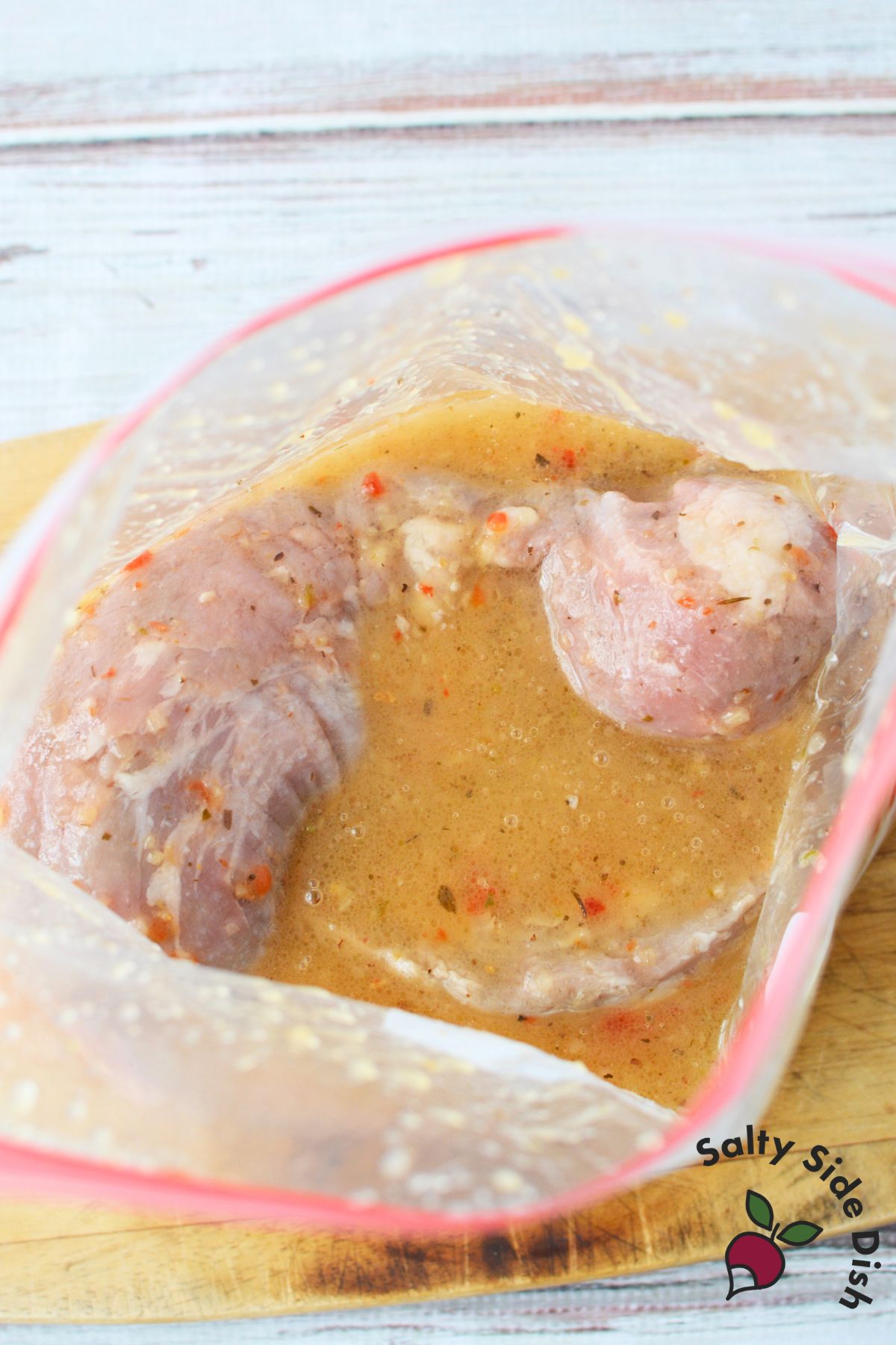 Raw pork tenderloin marinating in Italian dressing inside a resealable plastic bag.