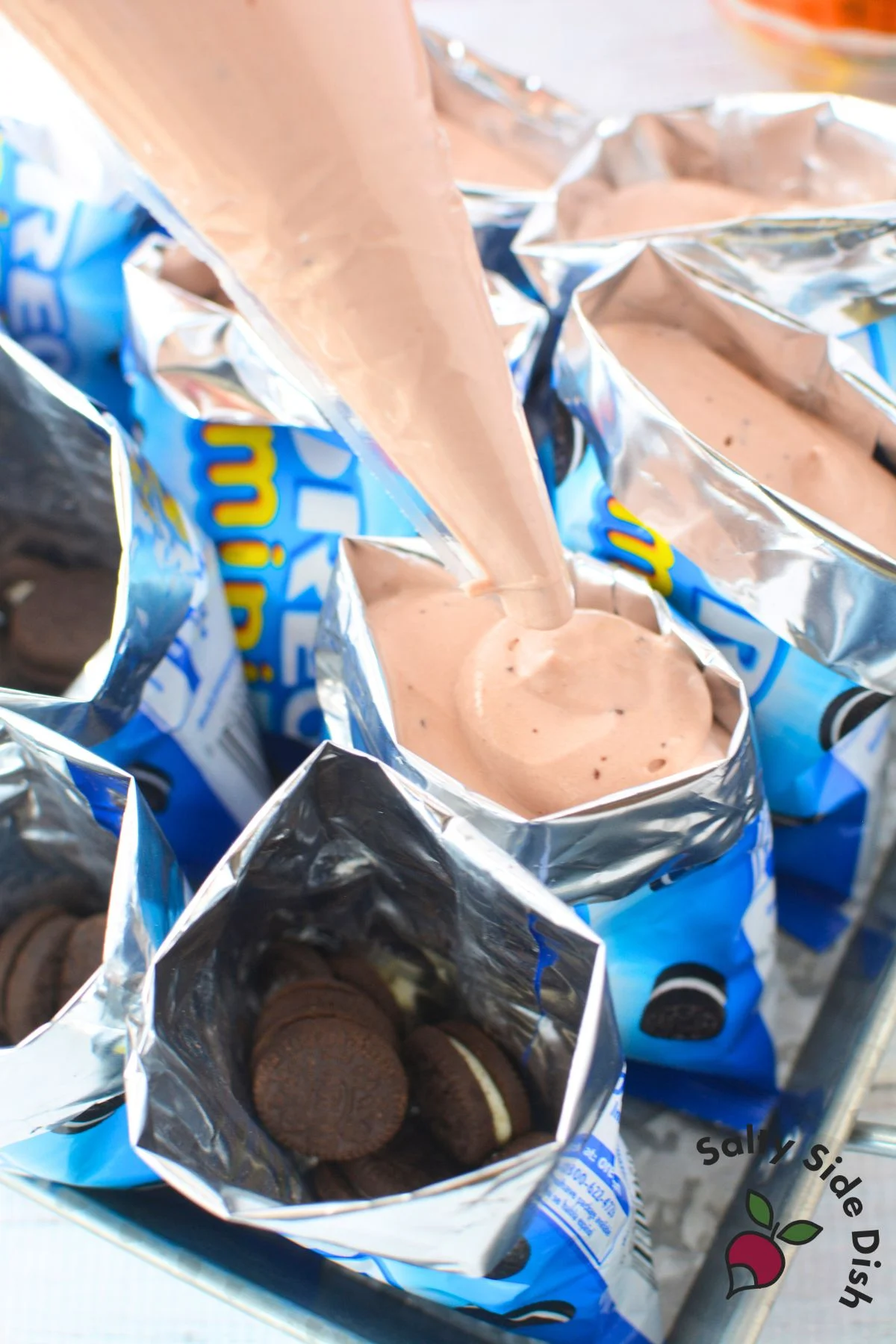 Chocolate pudding mixture being piped into mini Oreo bags to create walking dirt desserts.