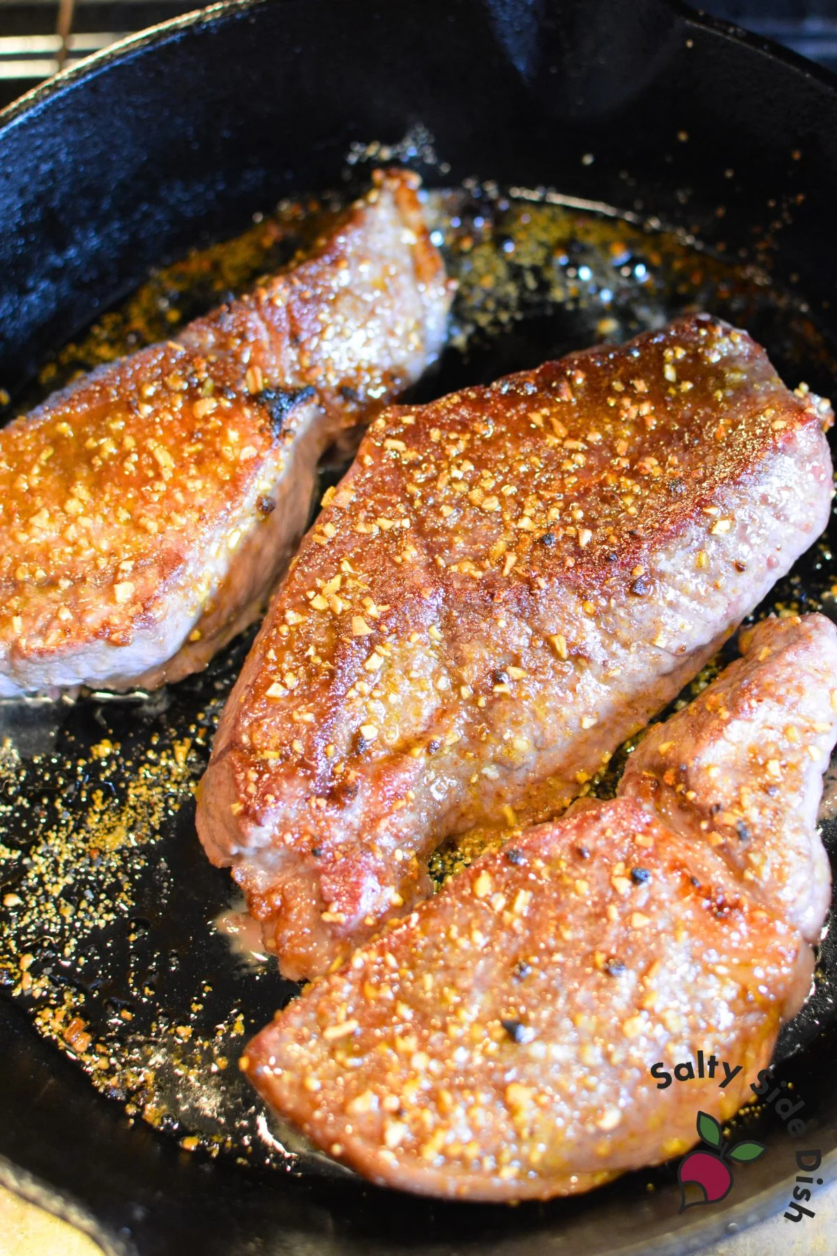 Broiled steaks sizzling in cast iron under the oven broiler.