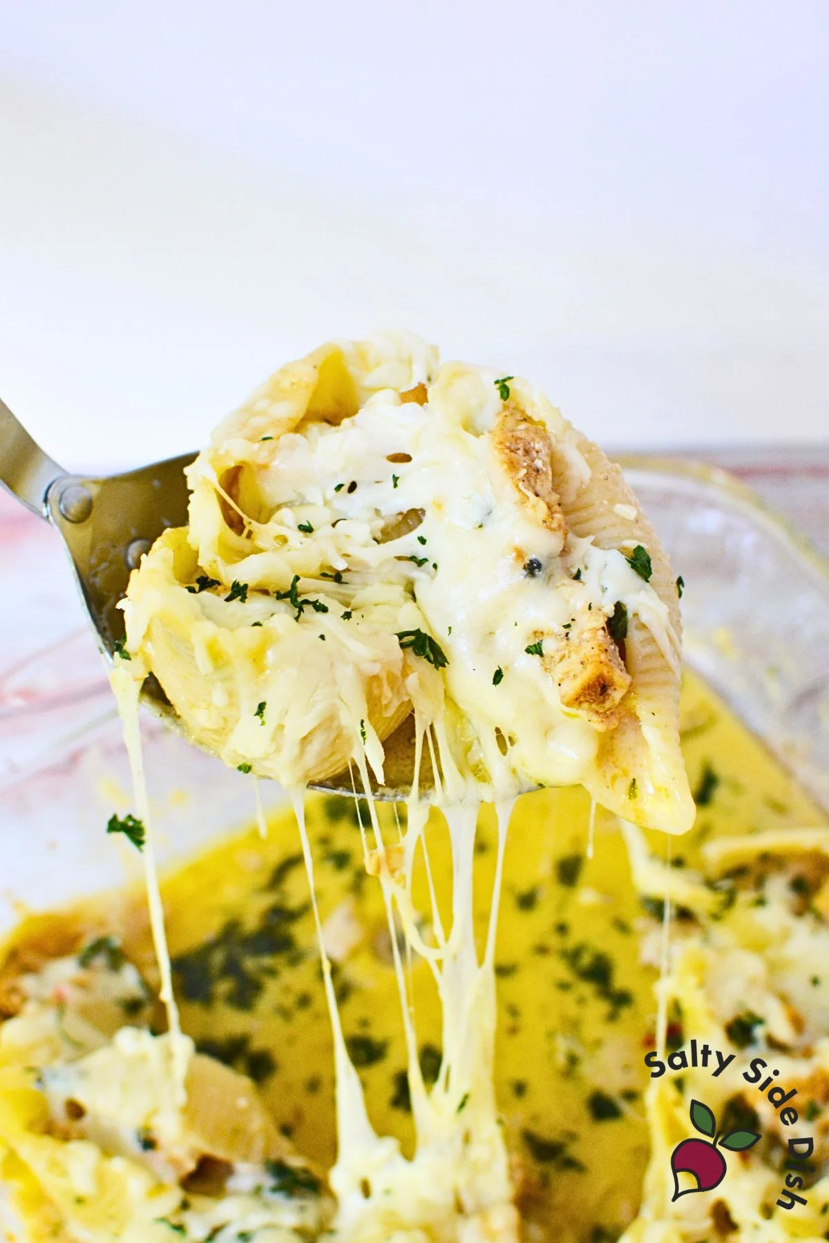 Close-up of a baked cheesy chicken Alfredo stuffed shell on a serving spoon, dripping with creamy sauce and mozzarella cheese.