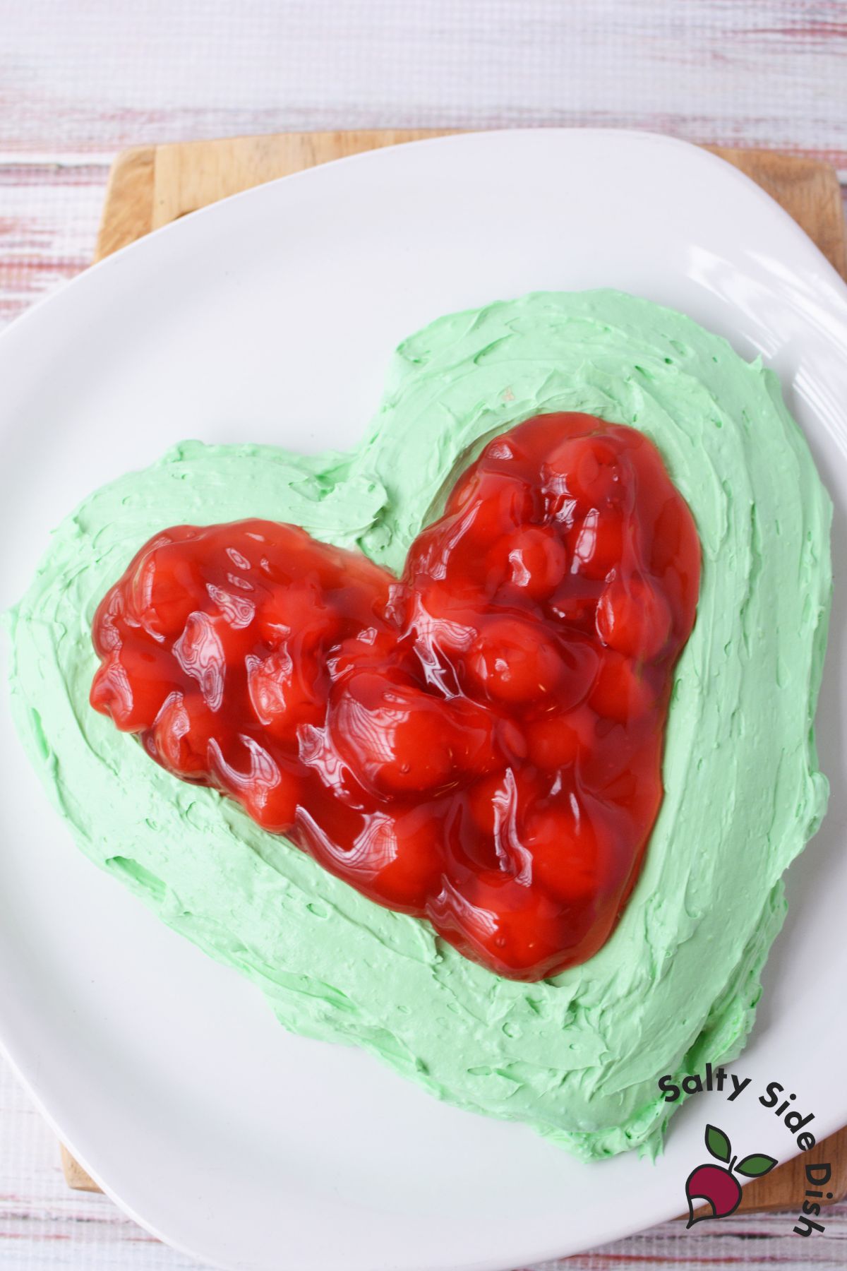 Cherry pie filling spread over heart-shaped green cheesecake dip on white platter