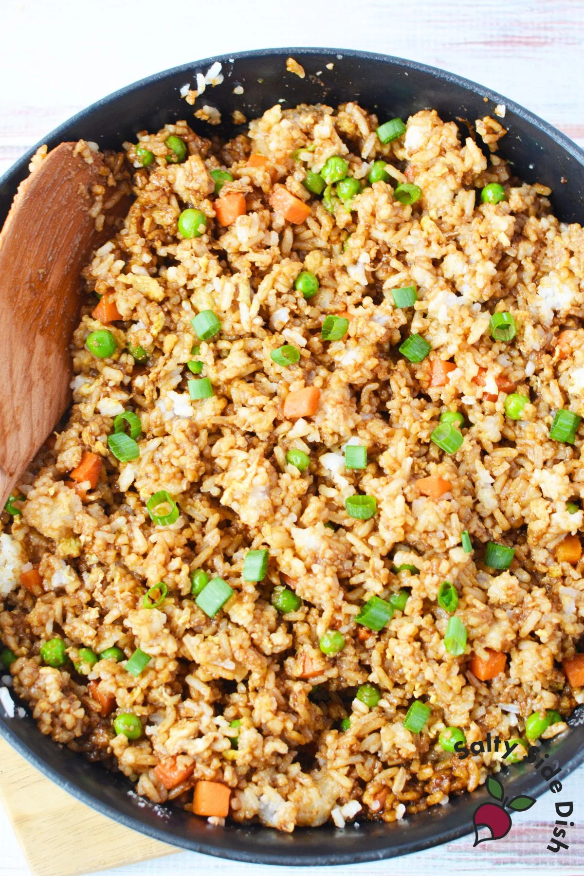 Jasmine fried rice with peas and carrots in a skillet with a wooden spoon